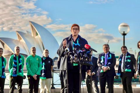 Photo of Minister Payne speaking at a press conference with several soccer players and officals standing behind the Minister. 